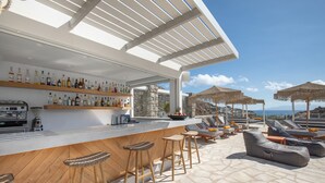 Un bar en la azotea con suelo de piedra, taburetes de bar de madera y sillones con sombrillas.