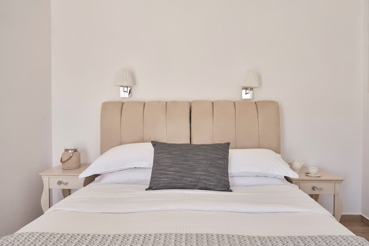 A bed with a headboard, two bedside tables, a lamp, a small container, and a cup.