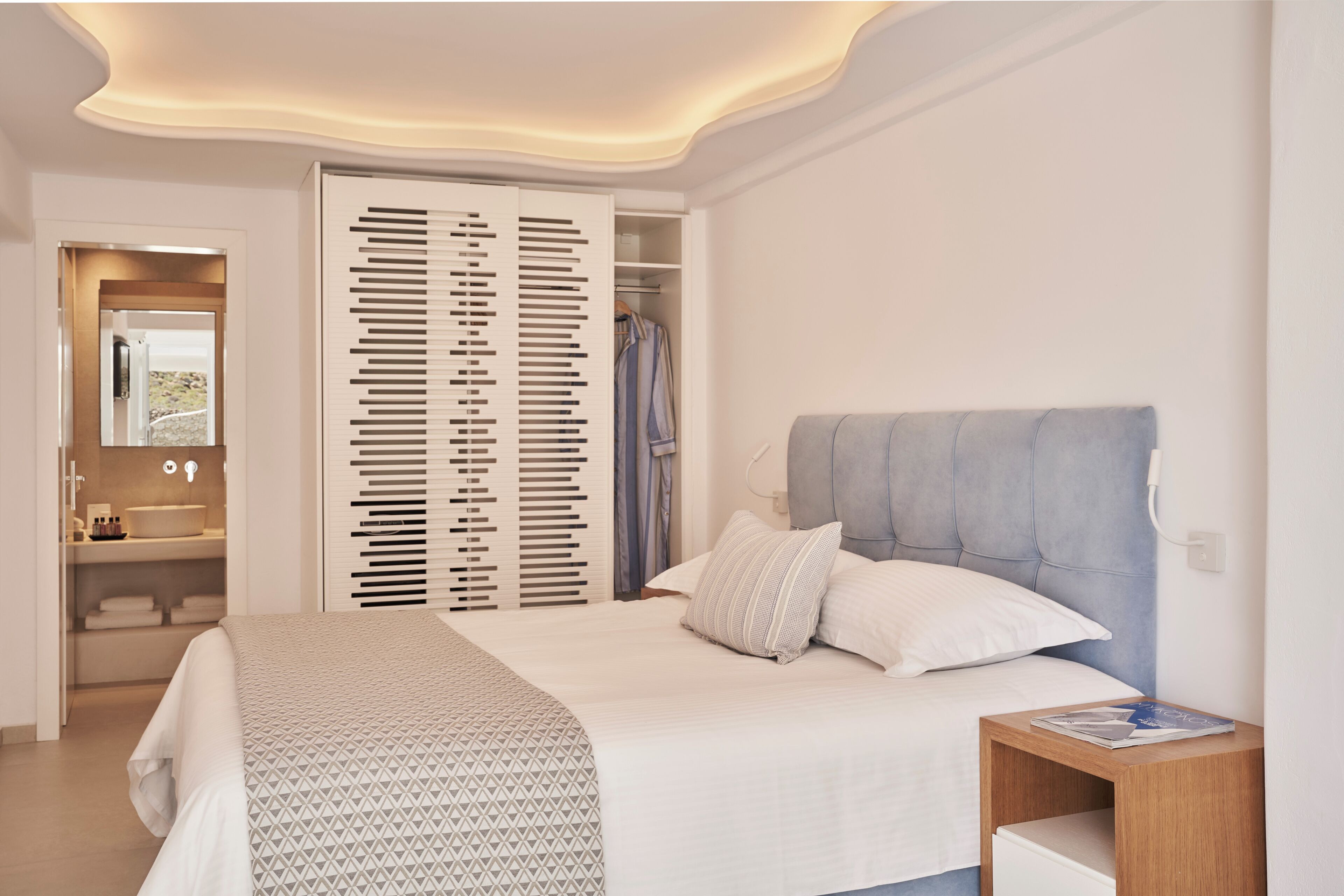 A modern bedroom with a large bed, a nightstand, a wardrobe, and a bathroom visible through an open door.