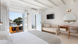Habitación de hotel con cama, escritorio, silla, televisor y vista a la piscina y palmeras.