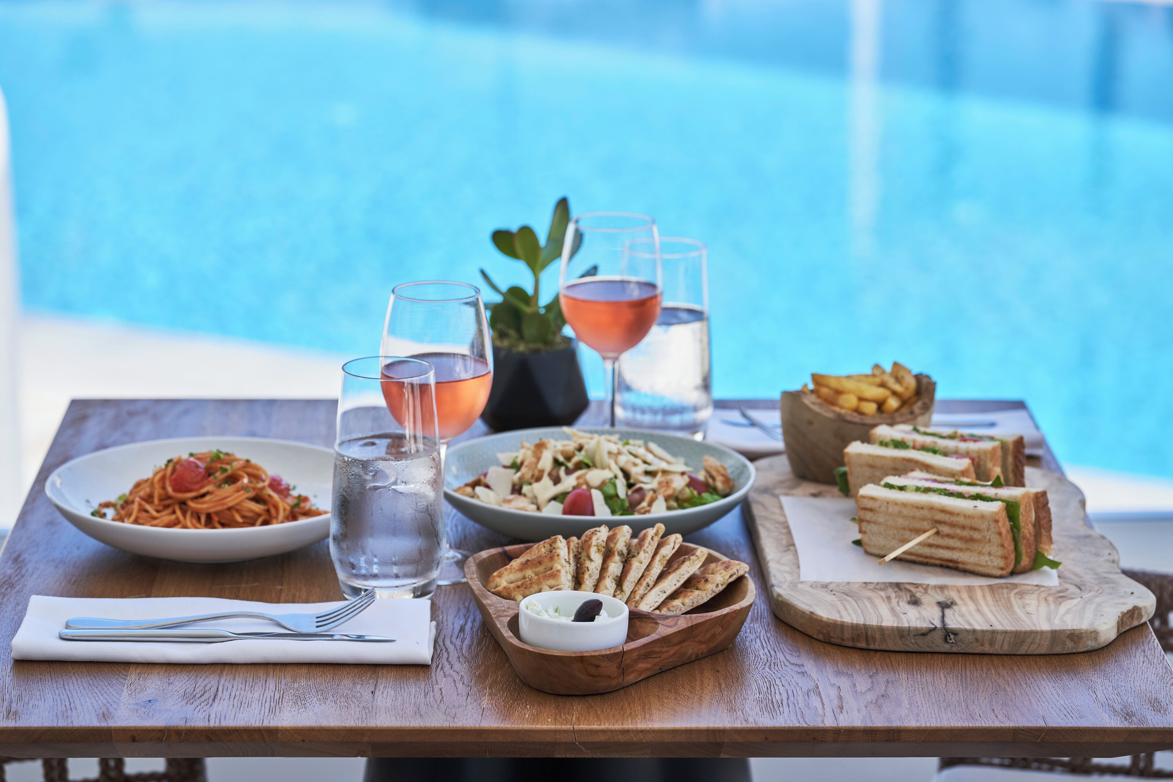 A dining table with a variety of dishes, including pasta, salad, and sandwiches, along with glasses of water and wine.