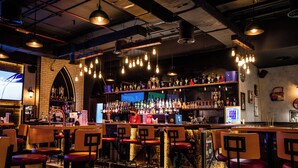 Un bar con varios taburetes, un cantinero y una estantería bien surtida con diferentes botellas.