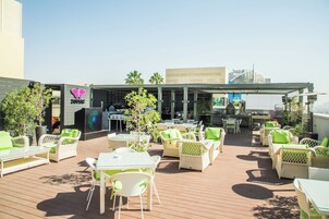 An outdoor patio area with wicker furniture, tables, and chairs, and a building with a sign in the background.
