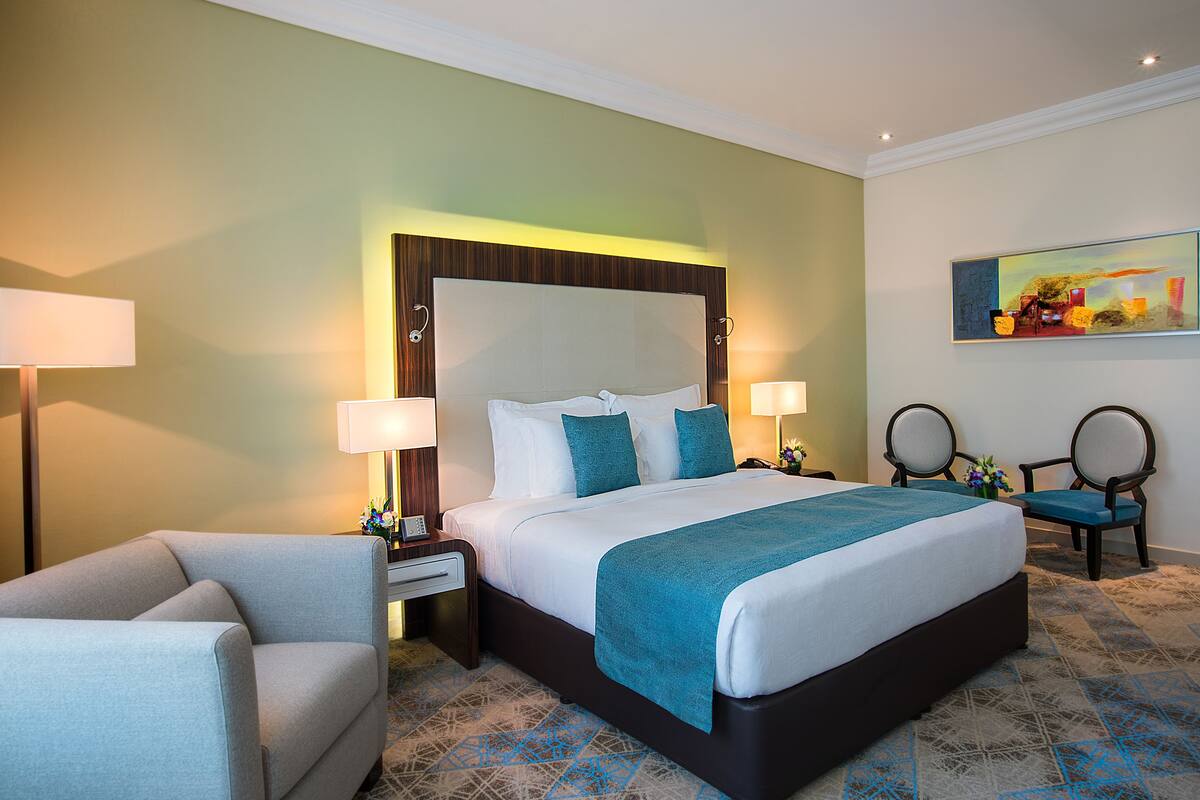 A hotel room with a large bed, two bedside tables with lamps, a chair, and a painting on the wall.