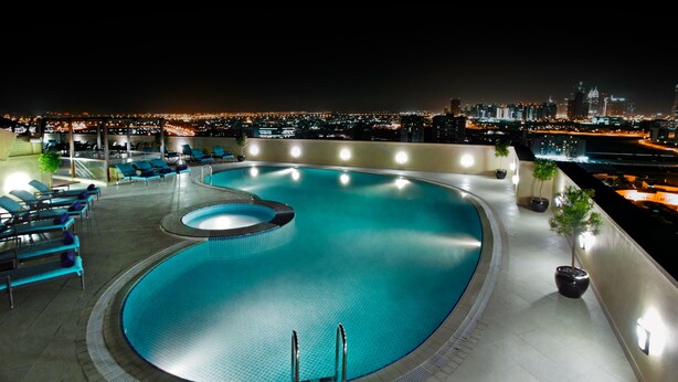 Una piscina en la azotea con sillones de descanso y vista nocturna de la ciudad.