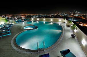A rooftop swimming pool with lounge chairs and a city view at night.