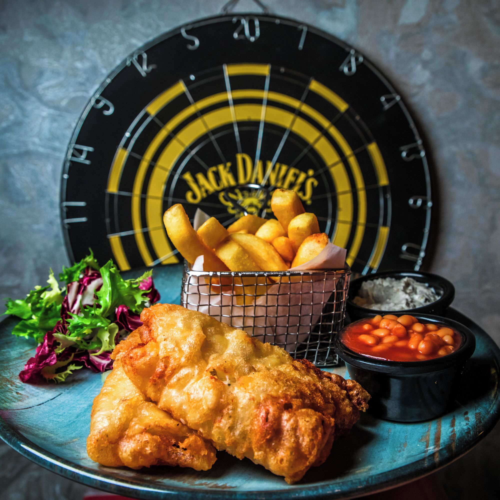 A plate with fried fish, a basket of fries, a salad, and two dipping sauces.
