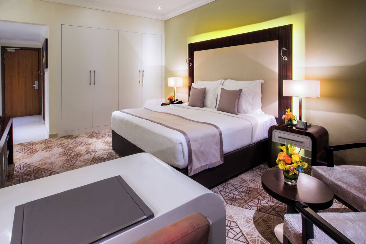 A hotel room with a large bed, bedside tables, a desk, and a wardrobe.