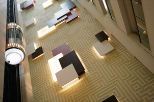 A modern lobby with geometric patterned walls, recessed lighting, and a glass elevator.