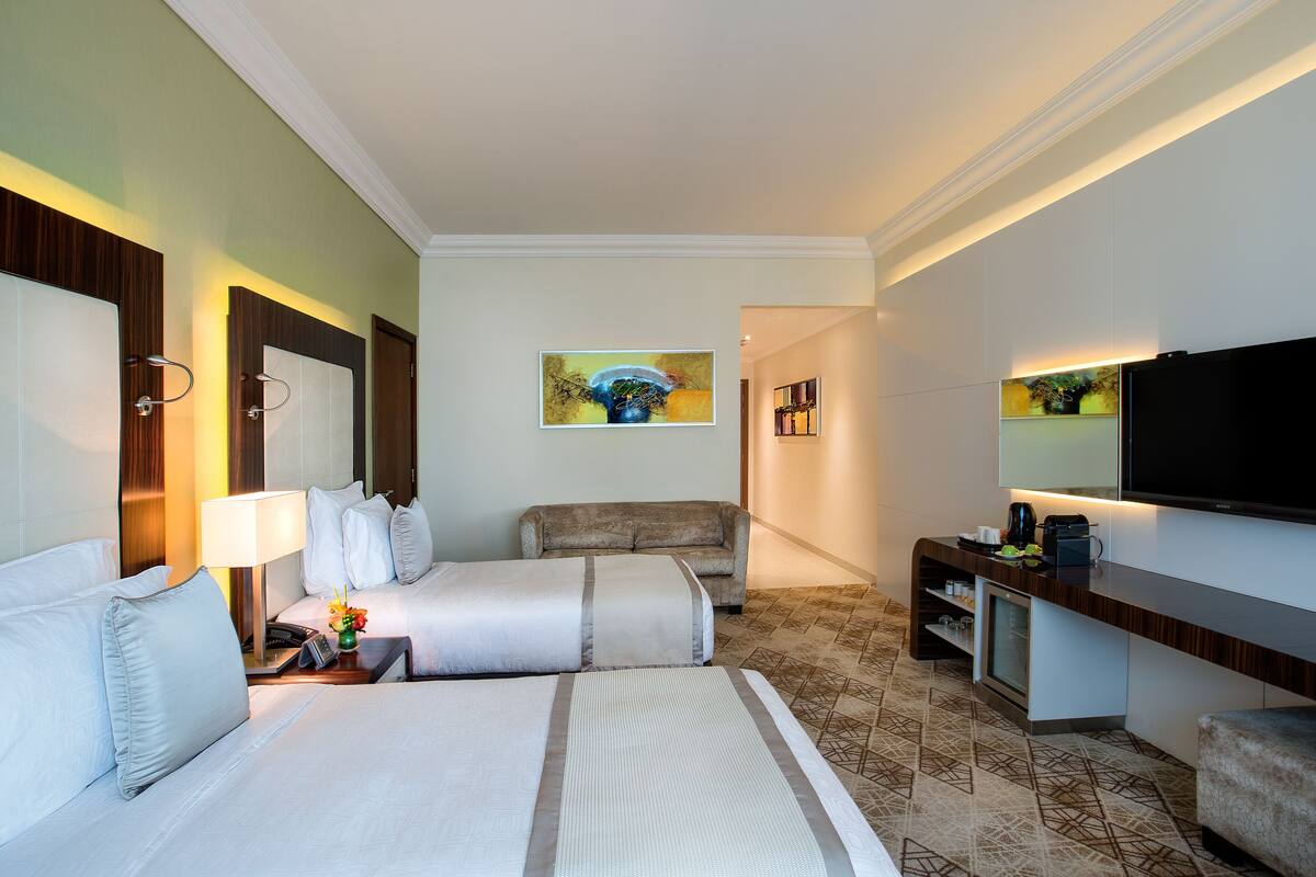 A hotel room with two beds, a sofa, a TV, and a minibar.