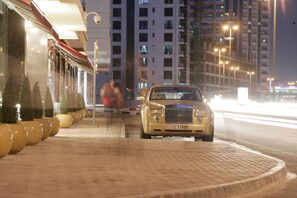 A luxury car parked on a brick-paved sidewalk next to a building with a red awning. - Elite Byblos Hotel (Dubai)