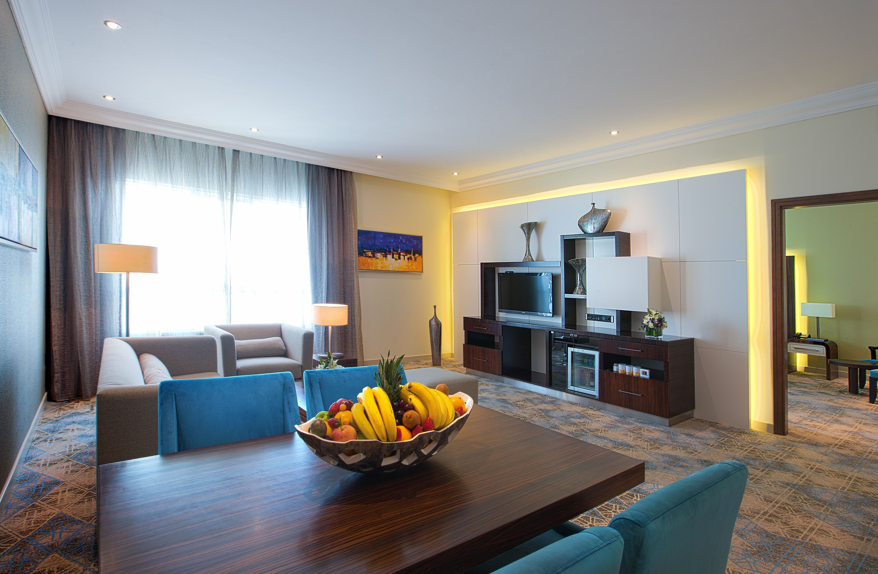 A hotel room with a dining area, a sofa, a TV, and a fruit bowl on the table.