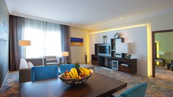 A hotel room with a dining area, a sofa, a TV, and a fruit bowl on the table.
