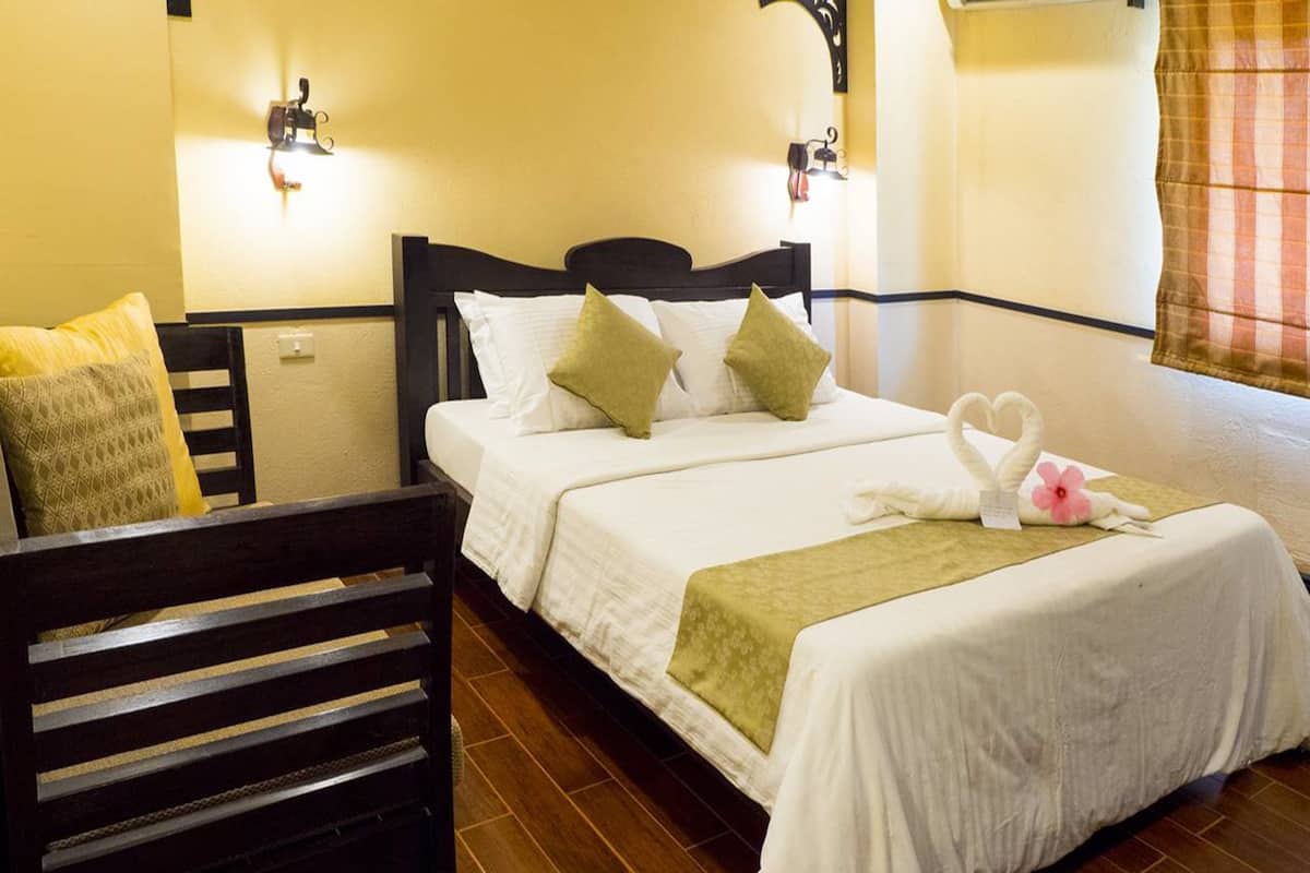 Una habitación de hotel con una cama, dos lámparas fijadas a la pared, un banco de madera y un cisne decorativo sobre la cama.