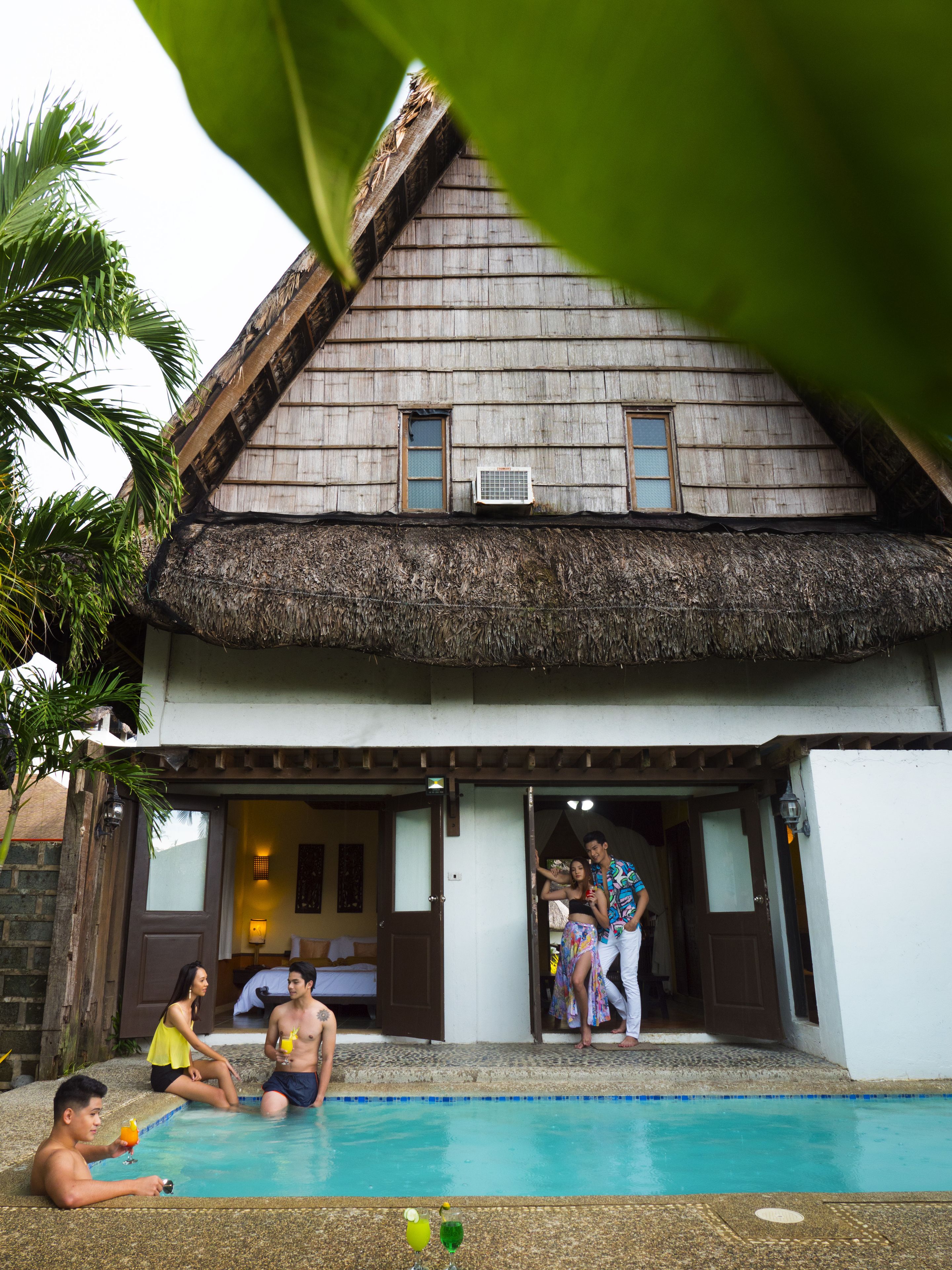 A thatched-roof house with a swimming pool, a wooden deck, and a small garden area.