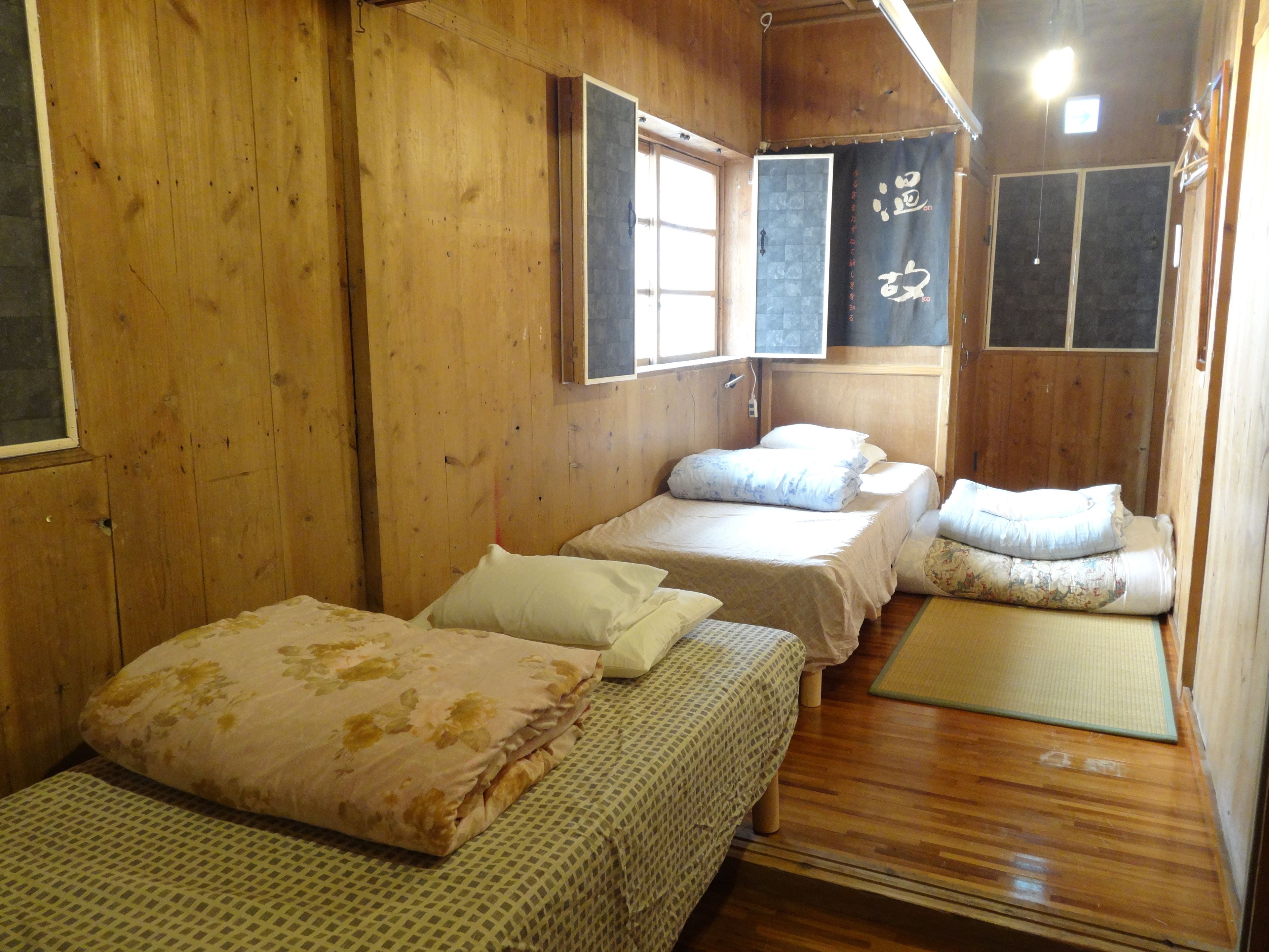 Una habitación de madera con dos camas, una ventana y un futón de tatami.