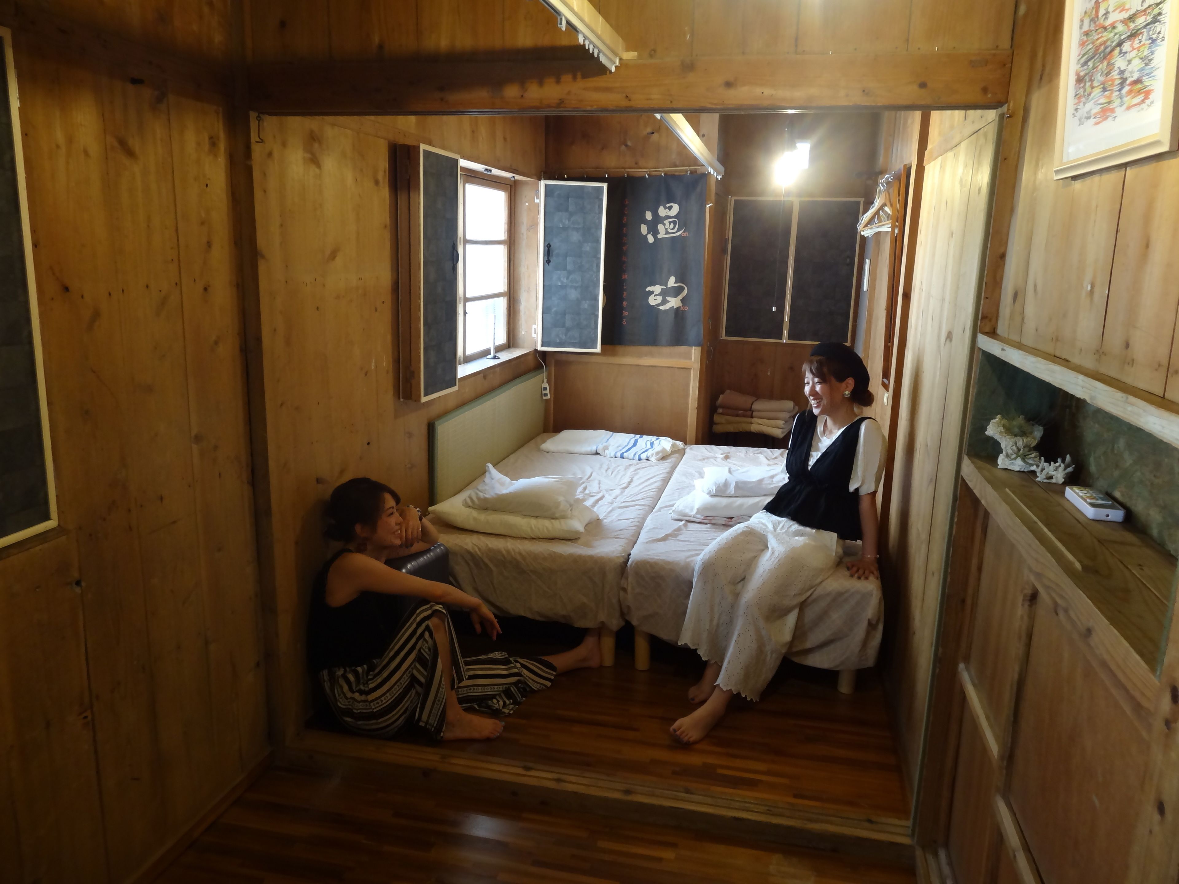 A wooden cabin room with two beds, a window, and a shelf with a decorative item.