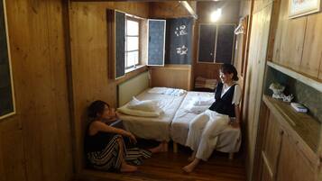 Una habitación de cabaña de madera con dos camas, una ventana y un estante con un adorno.