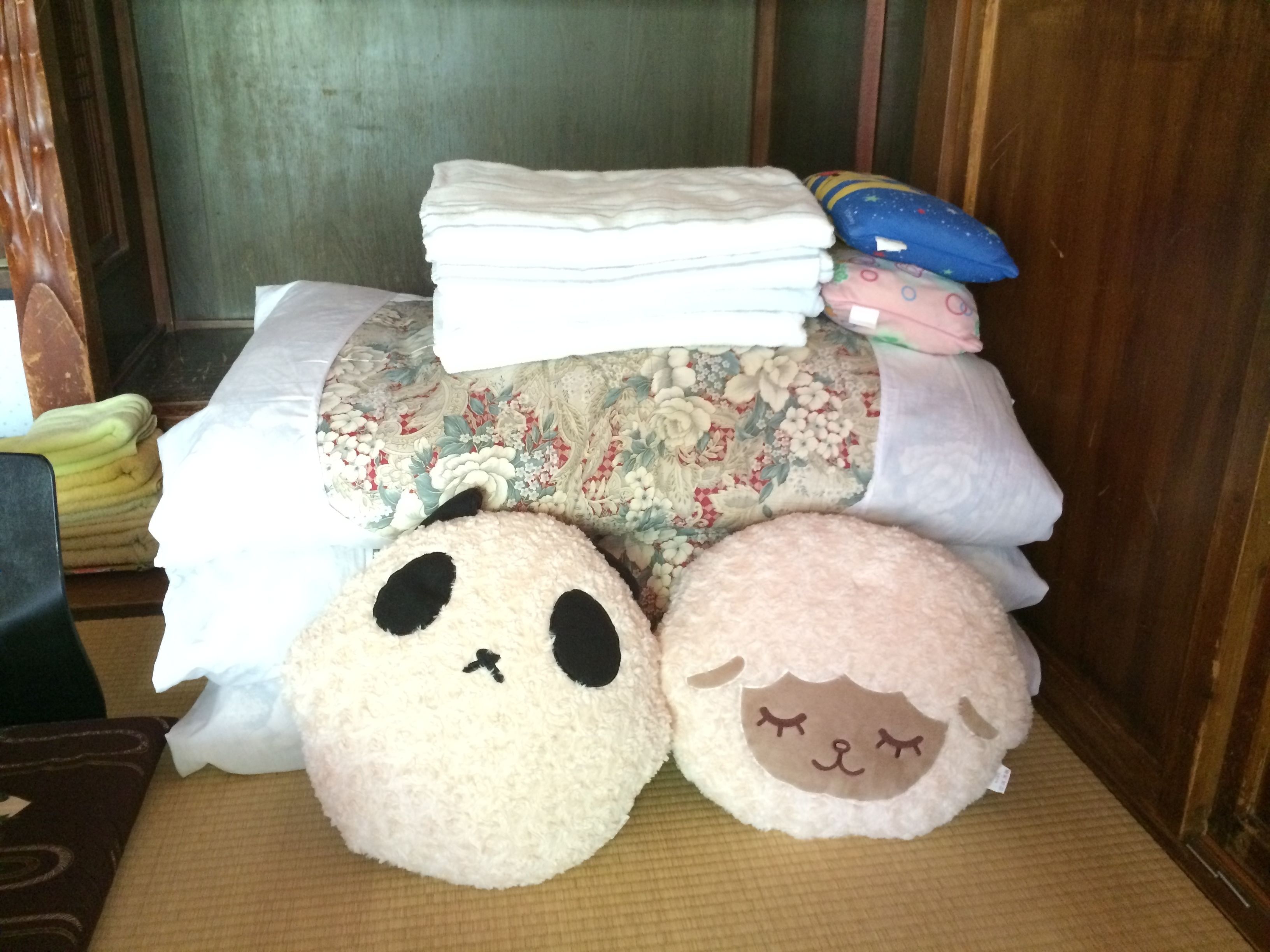 A bed with a floral-patterned bedspread, a stack of white pillows, and two plush toys on the floor.