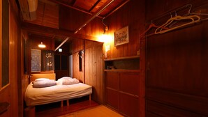 Una habitación pequeña y acogedora con paredes de madera y una cama. Se observa una estantería con objetos y una lámpara colgante.