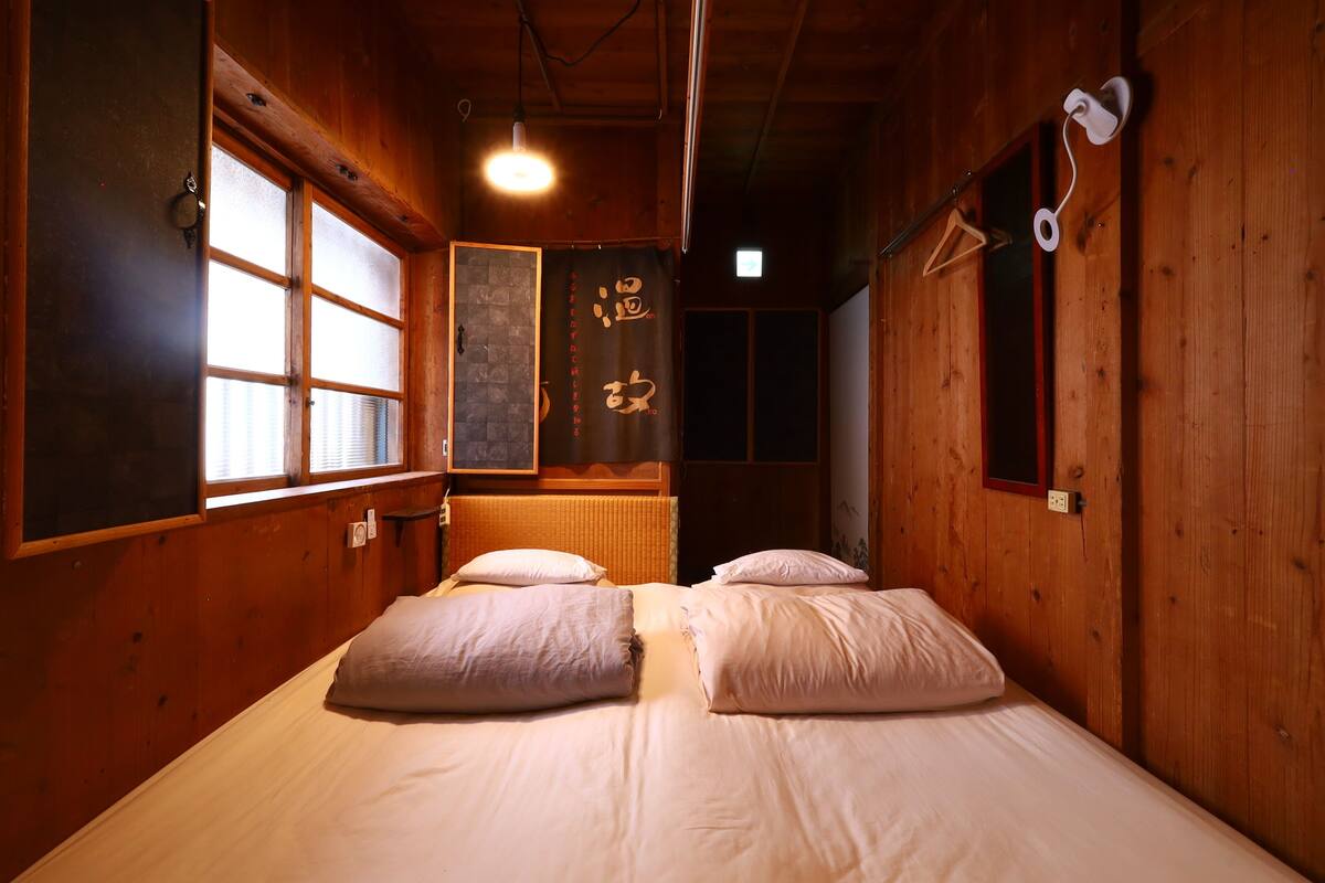 A wooden room with a bed, a window, and a wall-mounted light fixture.
