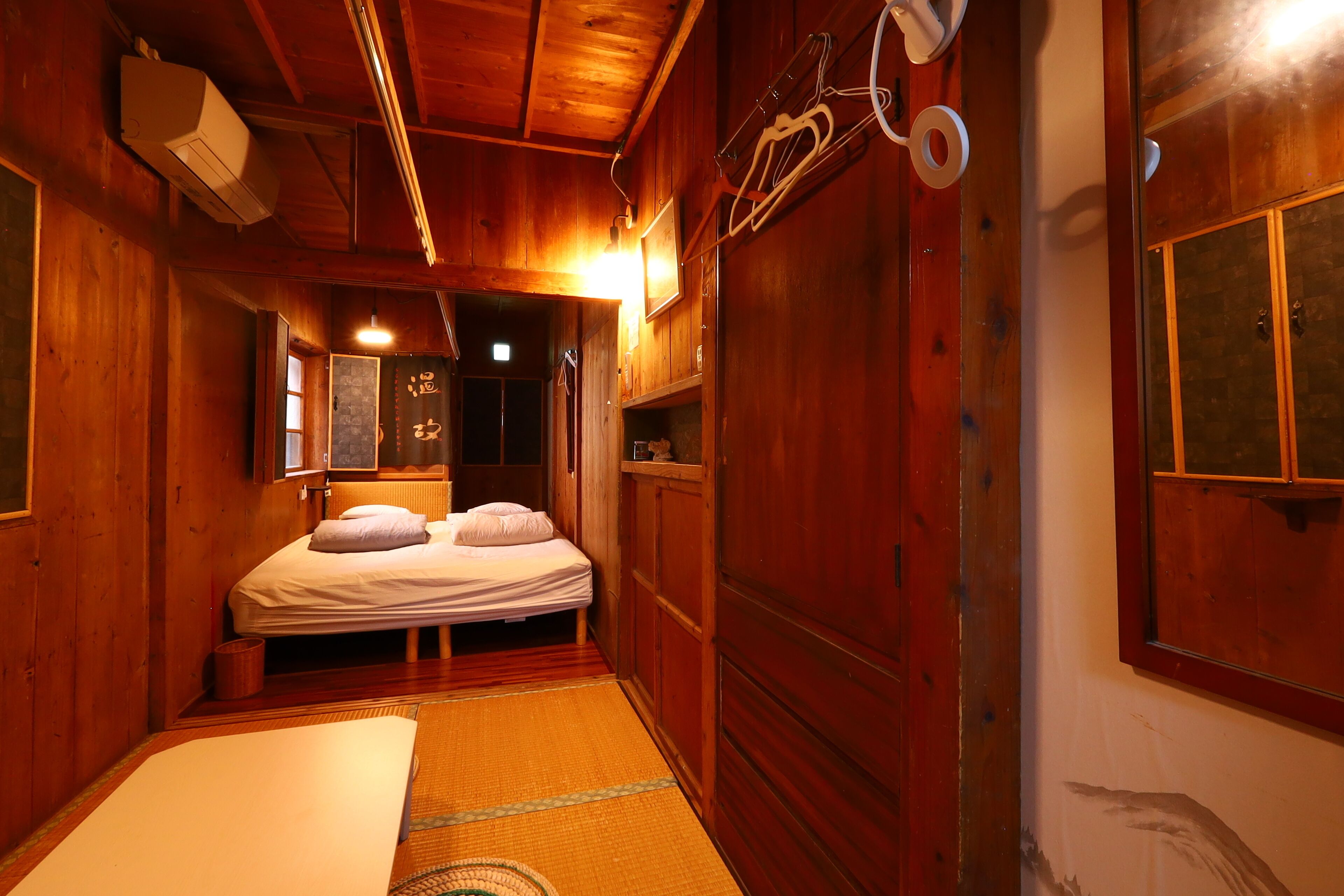 A wooden room with a bed, a small table, and a shelf with items.