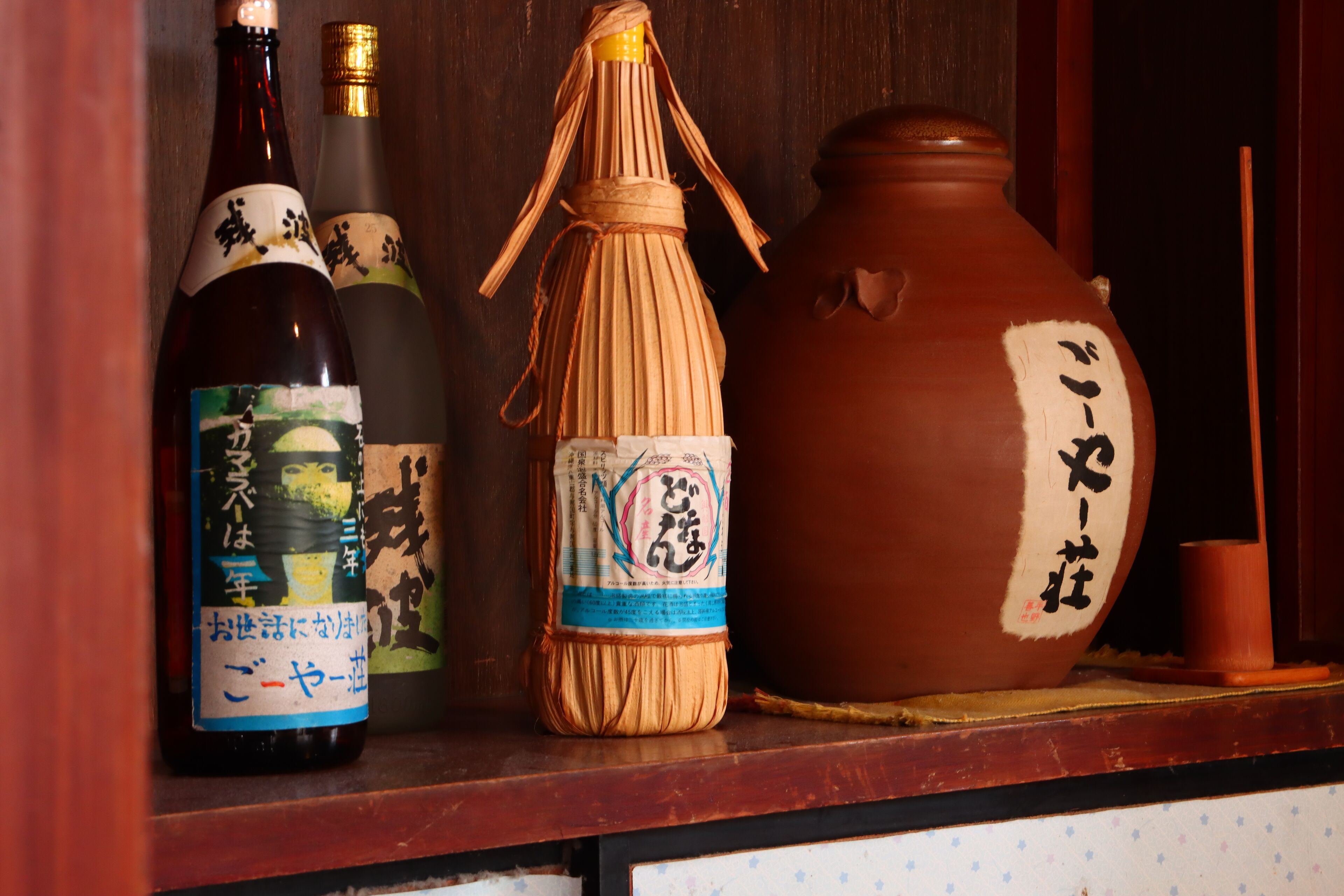 A shelf with three bottles and a ceramic pot, each with Japanese labels.