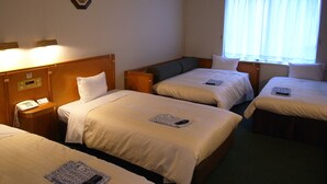 A hotel room with three single beds, each with a pillow and a remote control on it. There is a bedside table with a phone on it. - Hotel Kizankan (Tokyo)