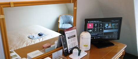 A hotel room with a bed, a desk with a computer, a telephone, and a mirror.