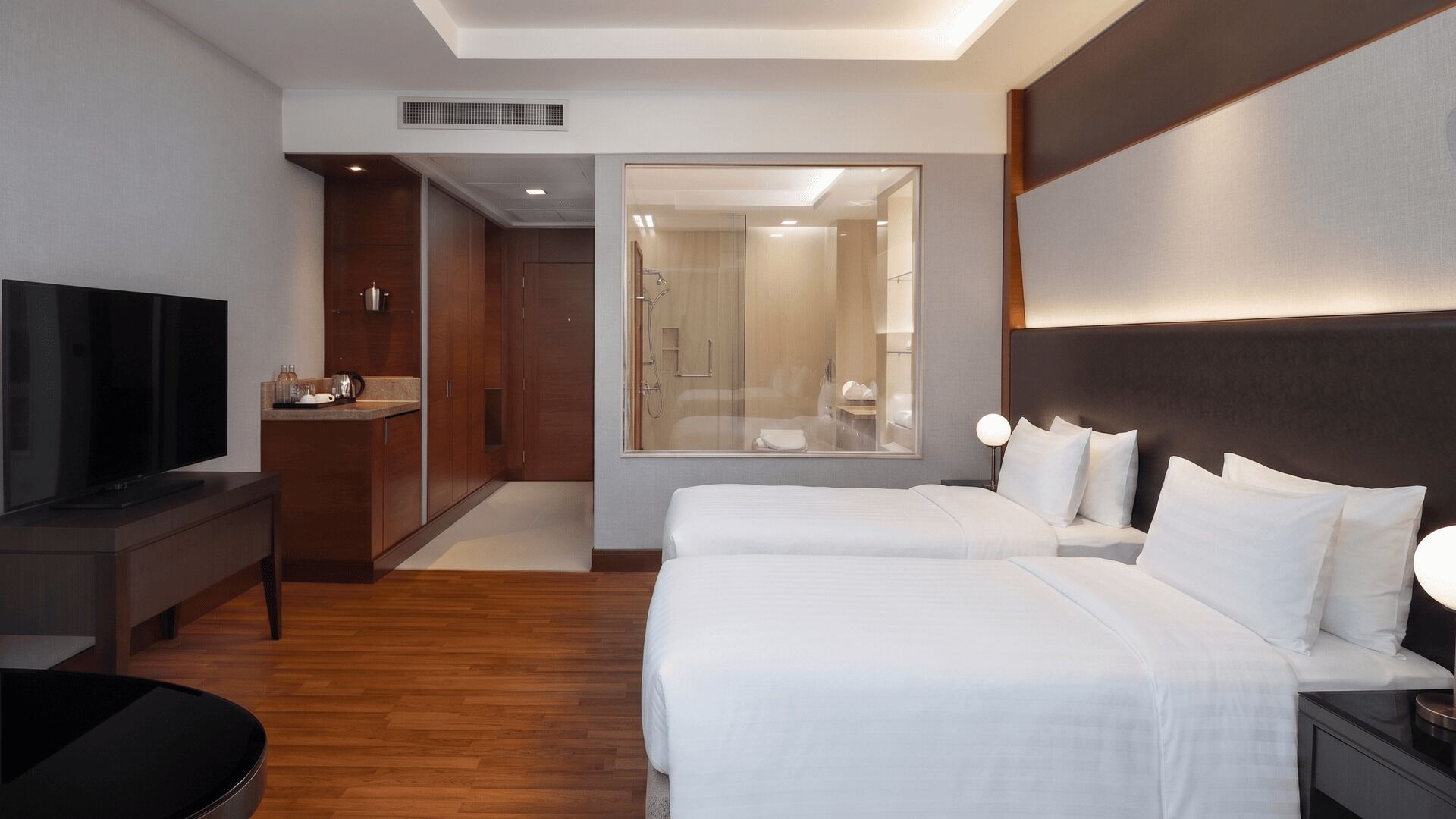 Camera d'albergo con televisore, scrivania, letto e bagno visibile attraverso una porta in vetro.