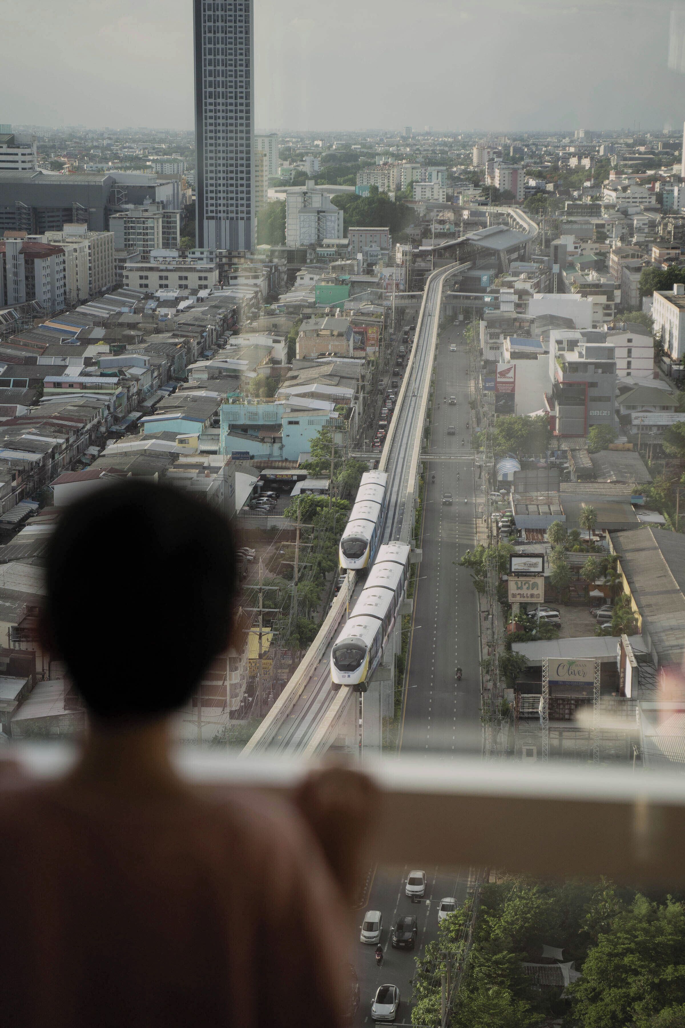 A cityscape with a high-rise building, a train track, and a person looking out from a window.