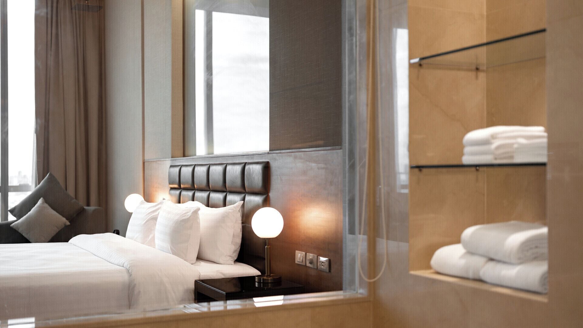 Una moderna camera d'hotel con un letto, abat-jour, comodini e vista sulla città attraverso ampie finestre.