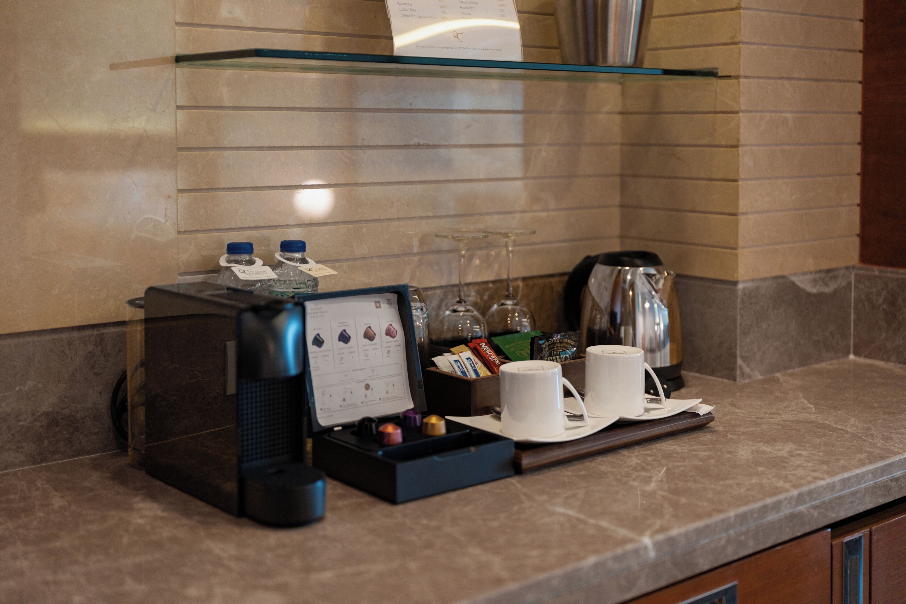 A coffee station with a coffee machine, cups, and a tray with various items.