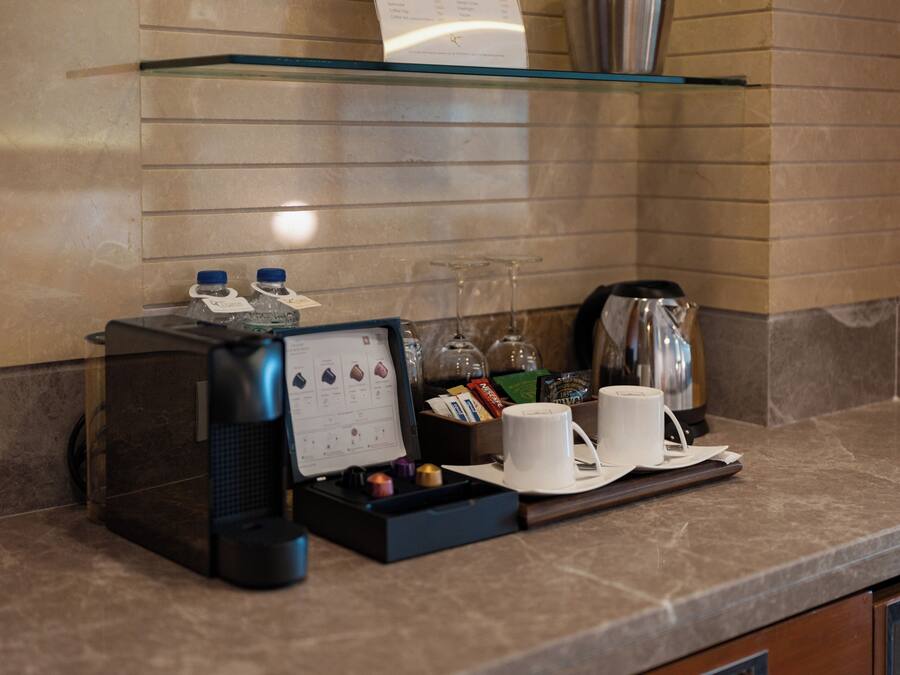 A coffee station with a coffee machine, cups, and a tray with various items.