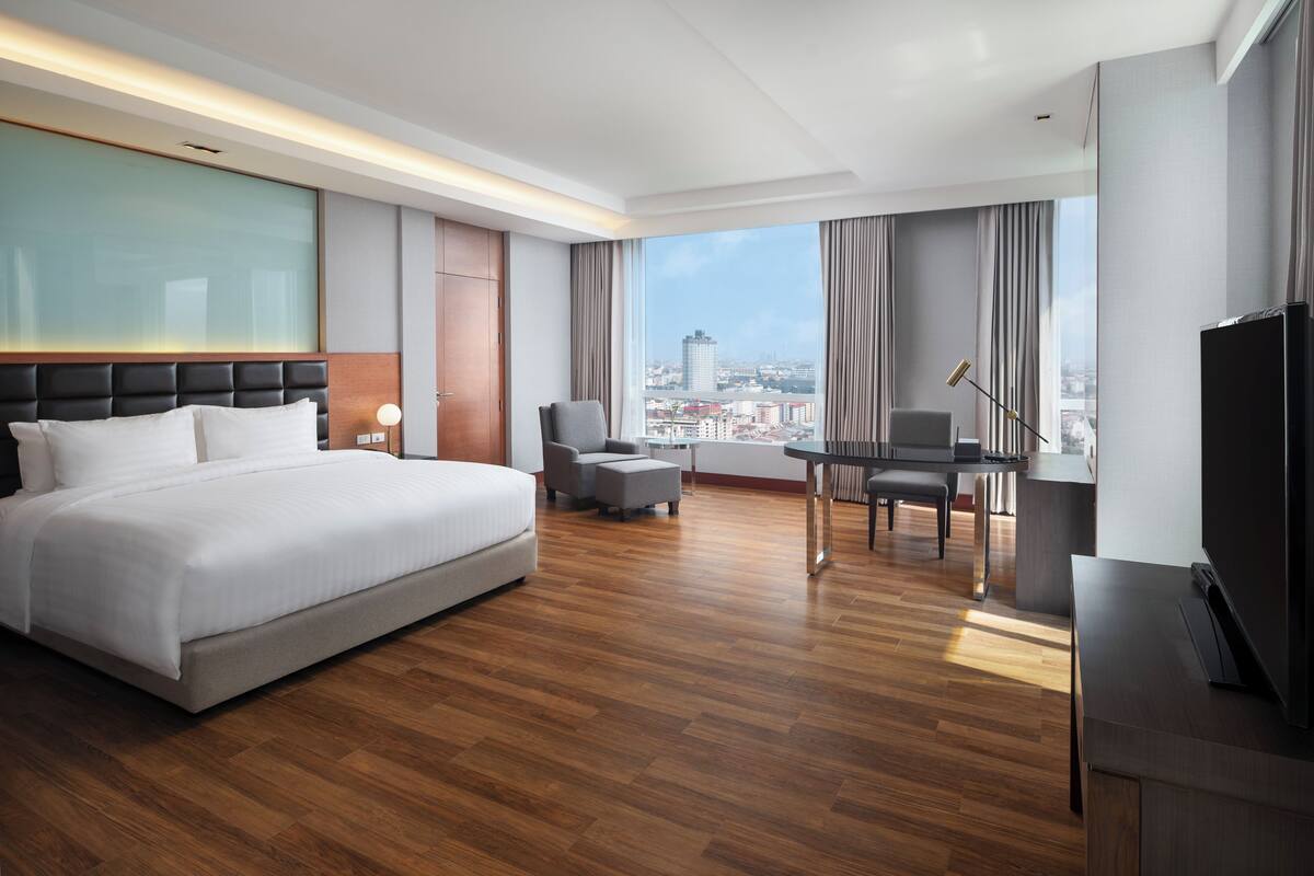 A hotel room with a large bed, a desk, a chair, and a TV.