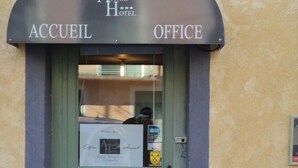 A hotel entrance with a green door, an archway labeled "Accueil" and "Office," and a sign indicating the hotel name.