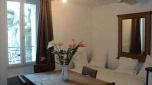 A room with a bed, a wooden table with a vase of flowers, a window with curtains, and a mirror on the wall.