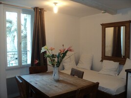Una habitación con una cama, una mesa de madera con un jarrón de flores, una ventana con cortinas y un espejo en la pared.