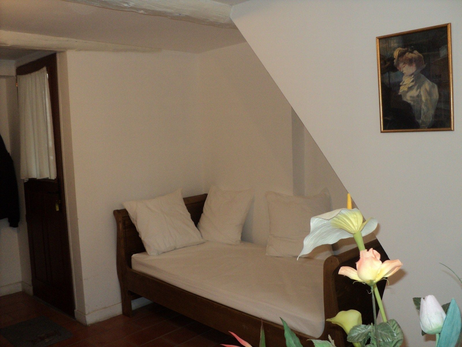 A small, cozy bedroom with a single bed, a wooden headboard, and a painting on the wall.
