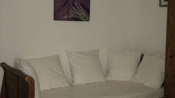 A room with a wooden bed frame, white bedding, and a painting of a field with trees on the wall.