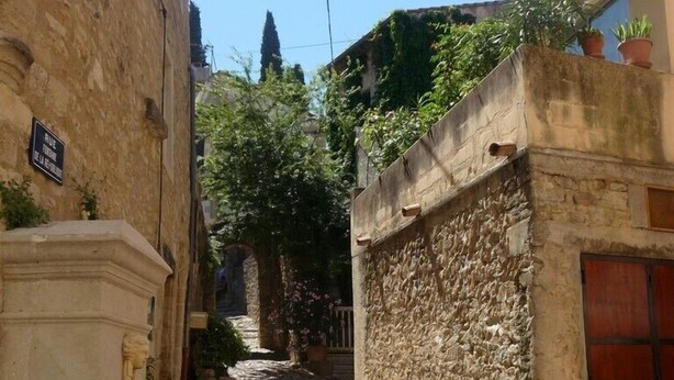 A narrow cobblestone alley flanked by stone buildings with a sign indicating 'Rue de la Fontaine'.