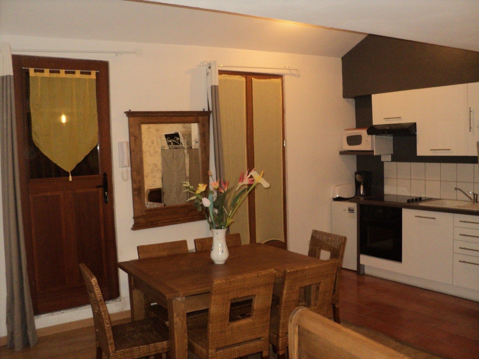 A compact kitchen with a dining area, wooden furniture, and a small white refrigerator.