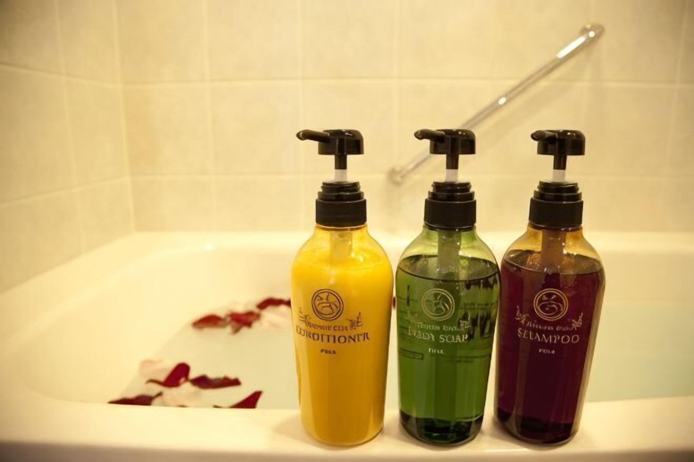 Three bottles of shampoo and conditioner on a bathtub.