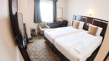 Una habitación de hotel con dos camas, un escritorio, una silla, un televisor y un ventanal con cortinas.