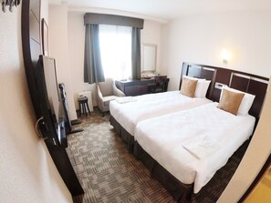 Ein Hotelzimmer mit zwei Betten, einem Schreibtisch, einem Sessel, einem Fernseher und einem Fenster mit Vorhängen.