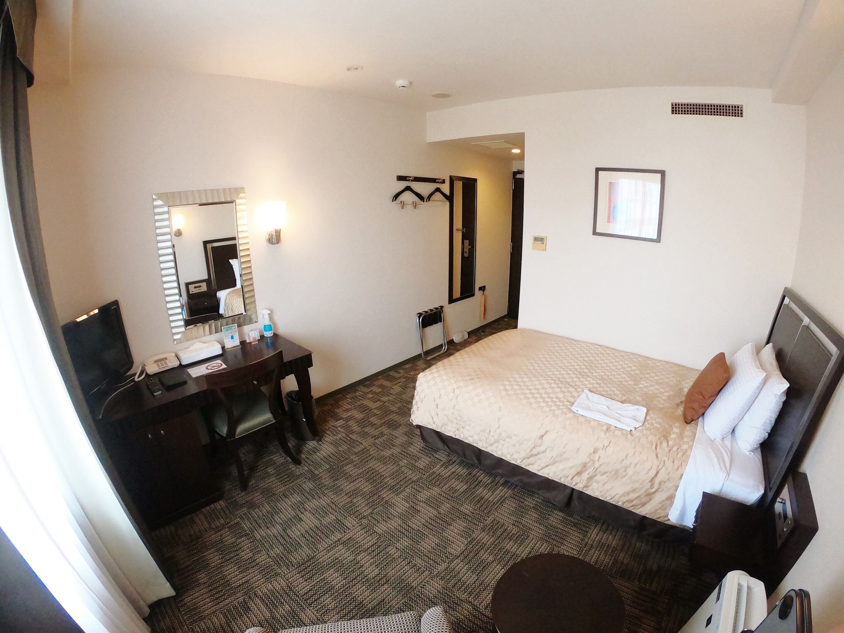 A hotel room with a bed, a desk with a telephone, a mirror, and a small round table.
