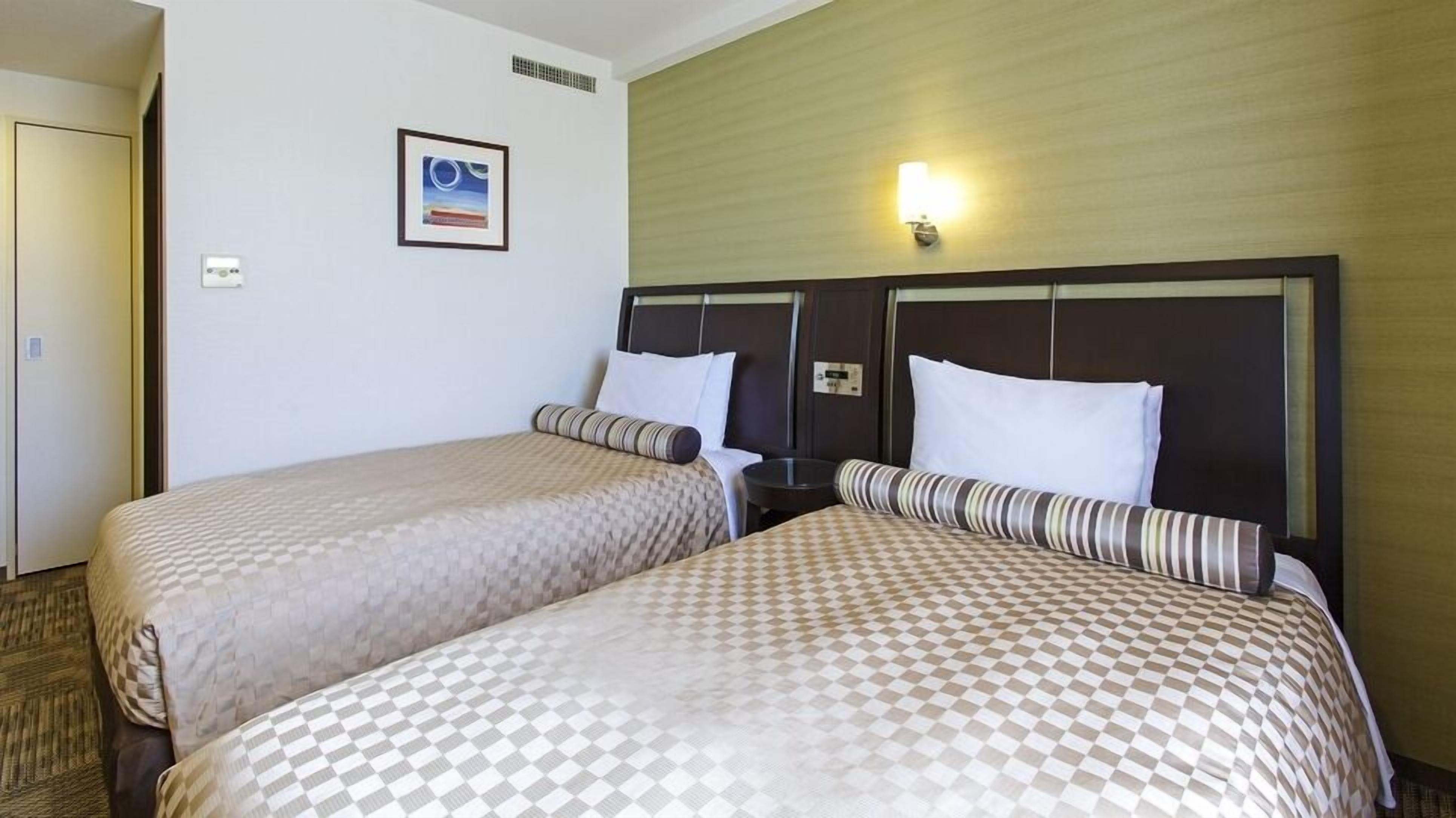 A hotel room with two beds, a framed picture on the wall, and a nightstand with a lamp.