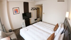 Ein Hotelzimmer mit einem großen Bett, einem an der Wand befestigten Flachbildfernseher, einem kleinen Nachttisch, einem Sessel und einem Spiegel.