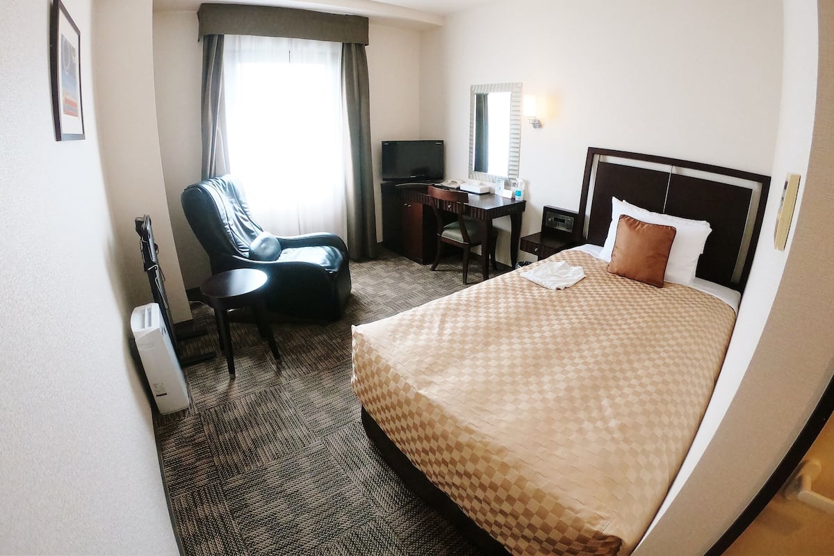 A hotel room with a bed, a desk, a chair, a TV, and a window with curtains.