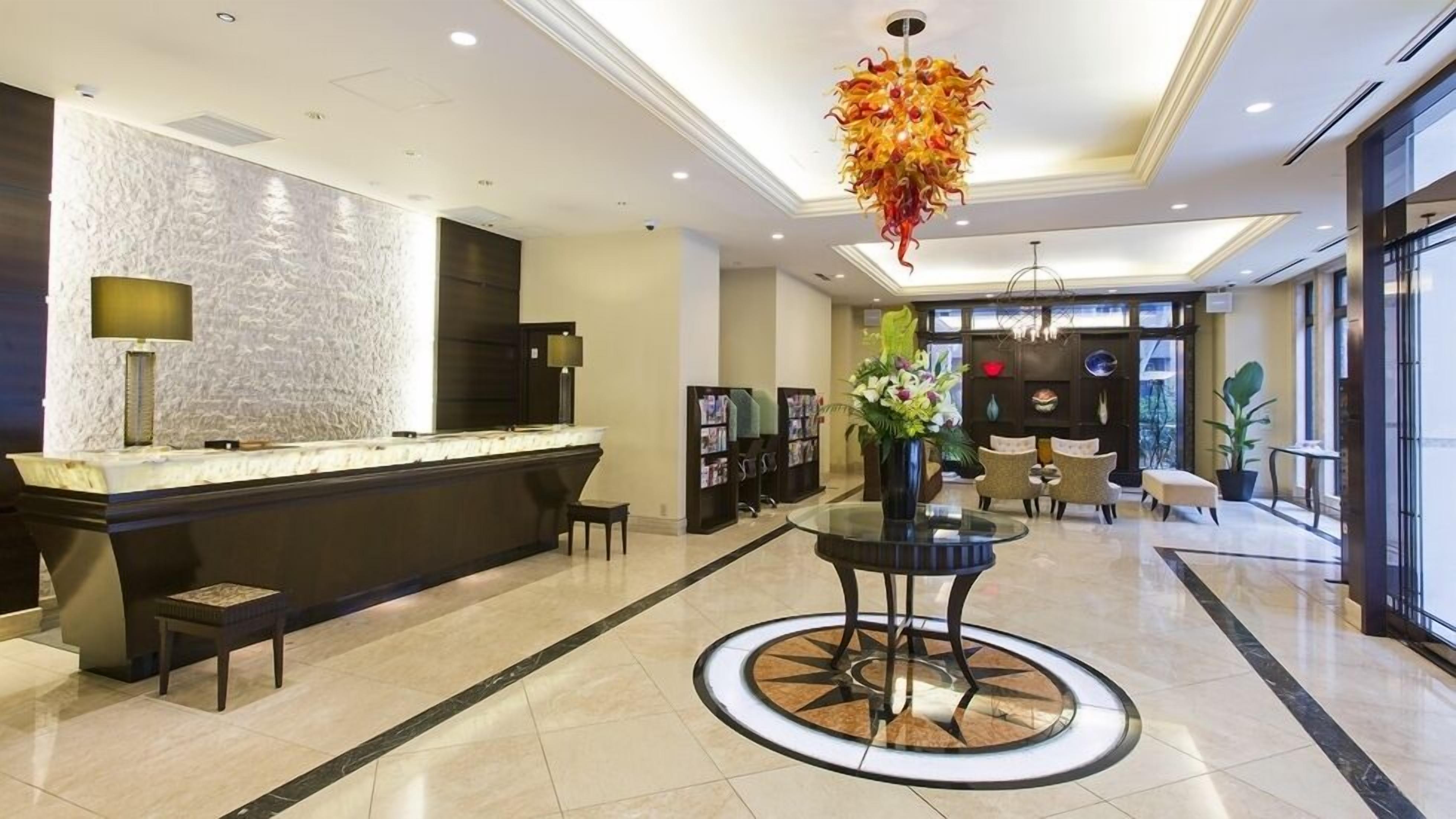 A hotel lobby with a reception desk, seating area, and a decorative glass chandelier.